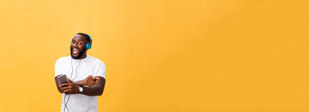 African American man with headphones listen and dance with music. Isolated on yellow background