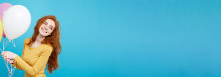 Celebrating Concept - Close up Portrait happy young beautiful attractive redhair girl smiling with colorful party balloon. Blue Pastel Background.の写真素材