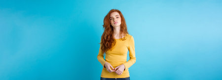 Portrait of young beautiful ginger woman with tender serious face crossing arms looking at camera. Isolated on pastel blue background. Copy space.の写真素材