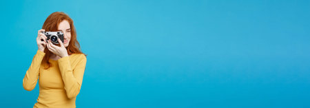 Travel and People Concept - Headshot Portrait of happy ginger red hair girl ready to travel with vintage camera in happy expression. Pastel blue background. Copy Space.の写真素材