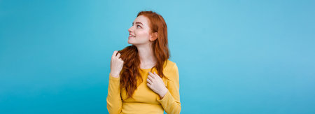 Portrait of happy ginger red hair girl with freckles smiling looking at camera. Pastel blue background. Copy Spaceの写真素材