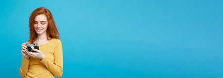 Travel and People Concept - Headshot Portrait of happy ginger red hair girl ready to travel with vintage camera in happy expression. Pastel blue background. Copy Space.の写真素材