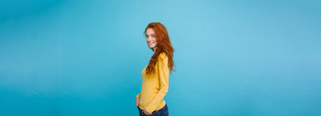 Lifestyle concept - Close up Portrait young beautiful attractive ginger red hair girl playing with her hair with shyness. Blue Pastel Background. Copy spaceの写真素材