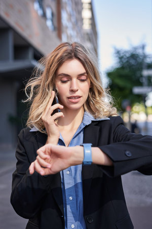 Portrait of confident businesswoman going on a meeting, standing on street, talking on mobile phone...