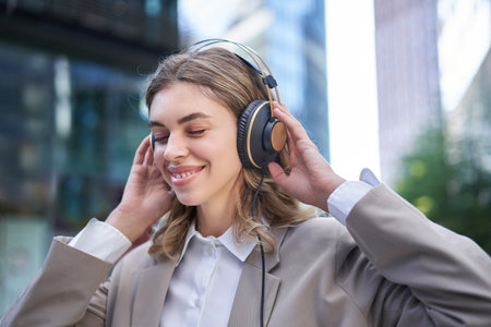 Happy businesswoman smiling, listening music in headphones while outside on streetの写真素材