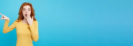 Close up Portrait young beautiful attractive redhair girl with shocking with something and pointing finger. Blue Pastel Background. Copy space.の写真素材