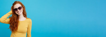 Travel concept - Close up Portrait young beautiful attractive ginger red hair girl with trendy sunglass smiling. Blue Pastel Background. Copy space.の写真素材