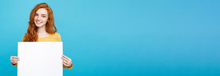 Business Concept -Close up Portrait young beautiful attractive ginger red hair girl smiling showing blank sign. Blue Pastel Background. Copy space.の写真素材