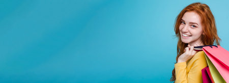 Shopping Concept - Close up Portrait young beautiful attractive redhair girl smiling looking at camera with shopping bag. Blue Pastel Background. Copy spaceの写真素材
