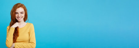 Lifestyle concept - Close up Portrait young beautiful attractive ginger red hair girl playing with her hair with shyness. Blue Pastel Background. Copy space.の写真素材