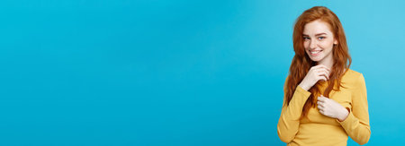 Lifestyle concept - Close up Portrait young beautiful attractive ginger red hair girl playing with her hair with shyness. Blue Pastel Background. Copy space.の写真素材