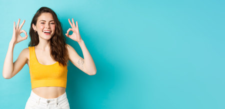 Young carefree woman say yes and nod in approval, showing okay gestures to praise good choice, show perfect body in summer outfit, ready for vacation, standing over blue backgroundの写真素材