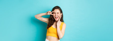 Excited girl screaming from joy, ready for summer holidays, showing v-sign and smiling happy, standing happy against blue backgroundの写真素材