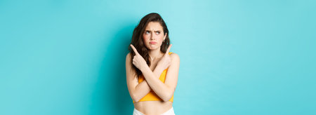 Young confused woman frowning perplexed, pointing fingers sideways and frowning displeased, need to choose, standing over blue backgroundの写真素材