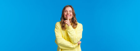 Happy cheerful silly blond caucasian woman in yellow hoodie hiding secret, prepare b-day surprise...