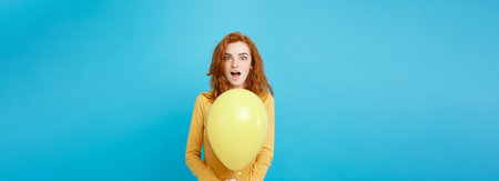 Celebrating Concept - Close up Portrait happy young beautiful attractive redhair girl smiling with colorful party balloon. Blue Pastel Background.の写真素材