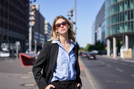 Portrait of corporate woman in suit and sunglasses, standing on street, looking confident and relaxedの写真素材