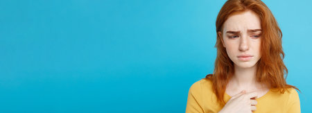 Headshot Portrait of tender redhead teenage girl with serious expression looking at camera. Caucasian woman model with ginger hair posing indoors.Pastel blue background. Copy Space.の写真素材