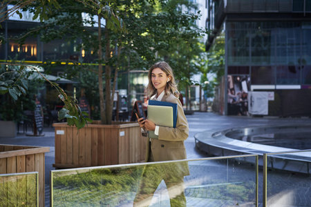 Beautiful smiling woman dressed in corporate suit, holding laptop and documents, smiling at camera