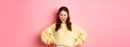 Sassy beautiful young woman, looking determined and self-assured, showing tongue, striking pose,...