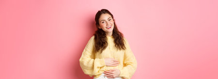 Young smiling woman touching her stomach with relieved, happy face, feeling good after eating...