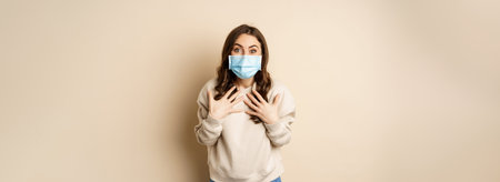 Covid-19, pandemic and quarantine concept. Surprised brunette woman in face medical mask, looking...