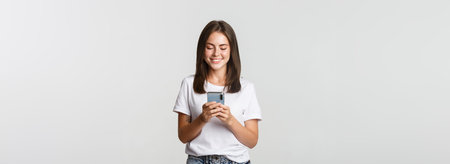 Smiling attractive girl using mobile phone and looking at screen pleased
