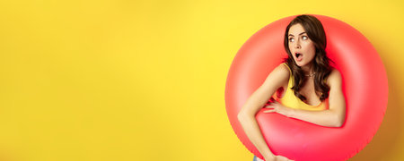 Close up portrait of coquettish young sexy woman inside pink swimming ring, concept of beach holiday, vacation and summer, yellow backgroundの写真素材