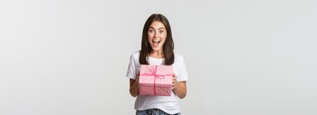 Surprised happy birthday girl receiving wrapped gift, white backgroundの写真素材