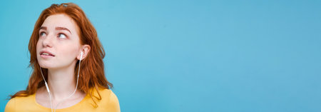 Lifestyle concept - Portrait of cheerful happy ginger red hair girl enjoy listening to music with headphones joyful smiling to camera. Isolated on Blue Pastel Background. Copy spaceの写真素材