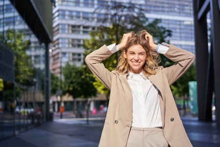 Stylish corporate woman, young lady boss in suit, looking confident and happy, posing outdoors on streetの写真素材