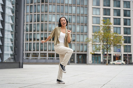 Happy people in city. Upbeat young girl dancing on street in headphones, listening music in headphonesの写真素材
