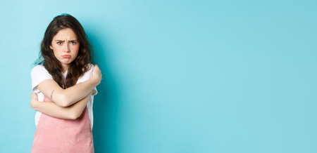 Sad and gloomy young woman pouting, comforting herself with cuddles, hugging her body and looking...