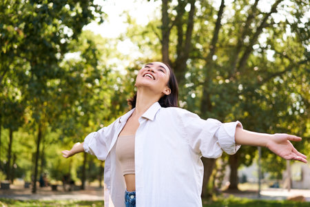 Portrait of carefree young asian woman dancing in park alone, enjoying freedom, smiling with joyの写真素材