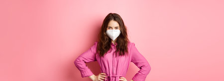 Covid-19, pandemic and lifestyle concept. Angry woman in medical respirator look with judgement and dislike, frowning and scolding someone without face mask, pink backgroundの写真素材