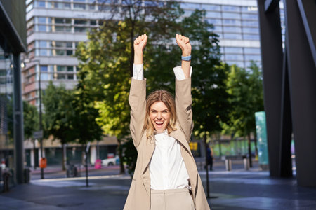 Portrait of successful business woman, young corporate woman celebrating victory, achievement, triumphing on street, making fist pumps and rejoicingの写真素材
