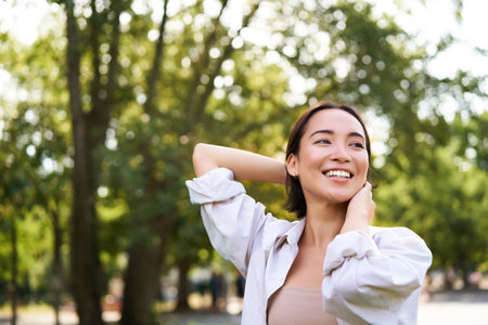 Women and beauty. Portrait of young happy asian woman walking on streets, enjoying stroll in park, smiling and looking aroundの写真素材