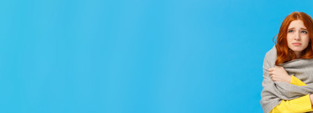 Girl sitting dormitory with broken heater, wrapping herself with warm scarf, looking upset and unwell upper left corner, grimacing suffer discomfort low temprature, catching cold, blue backgroundの写真素材