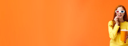 Interested and amused, smiling geeky redhead woman in yellow sweater, watching movie in cinema wearing 3d glasses, eating popcorn and stare curious with entertained and excited expressionの写真素材