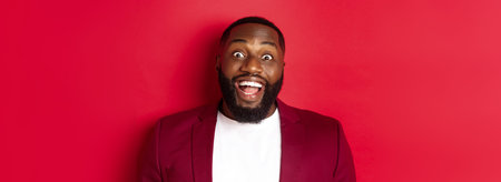 Close-up of african american man with beard staring amazed at camera, smiling and looking excited,...