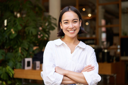 Portrait of smiling asian girl in white collar shirt, working in cafe, managing restaurant, looking confident and stylishの写真素材