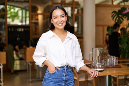 Portrait of young female entrepreneur, cafe owner, standing at the door entrance and smiling, looking confidentの写真素材