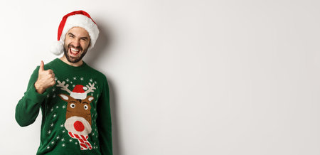 Christmas holidays, celebration and party concept. Man enjoying New Year, showing thumb up in approval, wearing Santa hat, white backgroundの写真素材