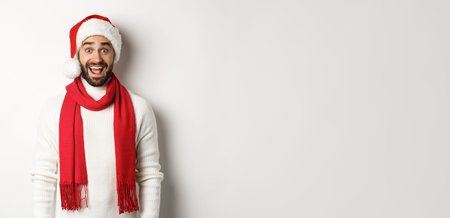 Christmas holidays. Bearded man looking surprised at camera, wearing santa party hat and red scarf,...