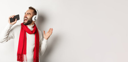 Winter holidays and technology concept. Man playing karaoke app on mobile phone, singing in...