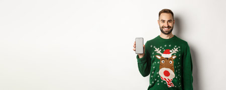 New Year, online shopping concept. Smiling bearded man showing Christmas offer on mobile screen,...