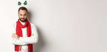 Christmas party and celebration concept. Suspicious young bearded man looking doubtful, wearing funny accessory hat, standing against white backgroundの写真素材