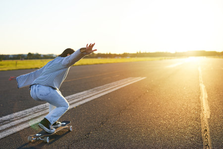 Happy skater girl riding her skateboard and having fun on empty street. Smiling woman enjoying cruiser ride on sunny roadの写真素材