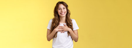Girl thanking gladly awesome opportunity part of team smiling grateful press palms heart grinning tilt head lovely amused thankful gaze camera delighted stand yellow backgroundの写真素材