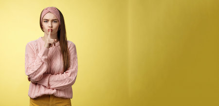 Keep mouth shut. Serious-looking bossy attractive young 20s woman in sweater, headband shushing...